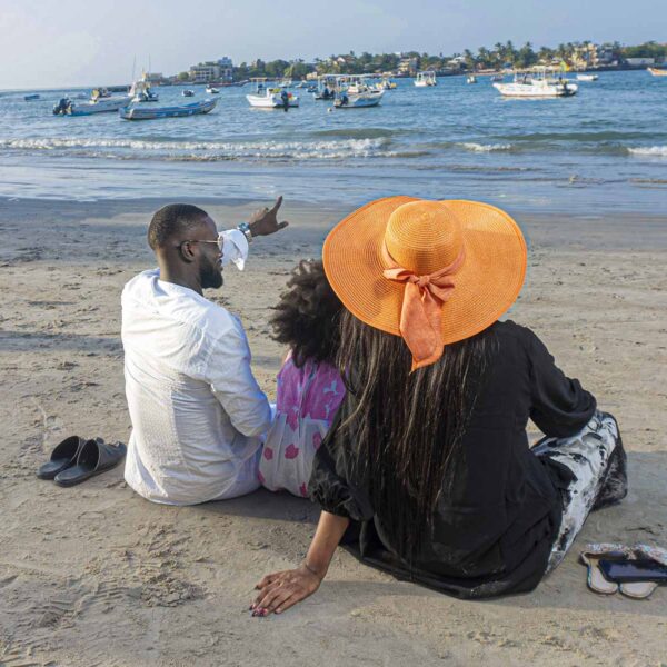 un homme et une femme sont assis sur la plage et la femme porte un chapeau orange