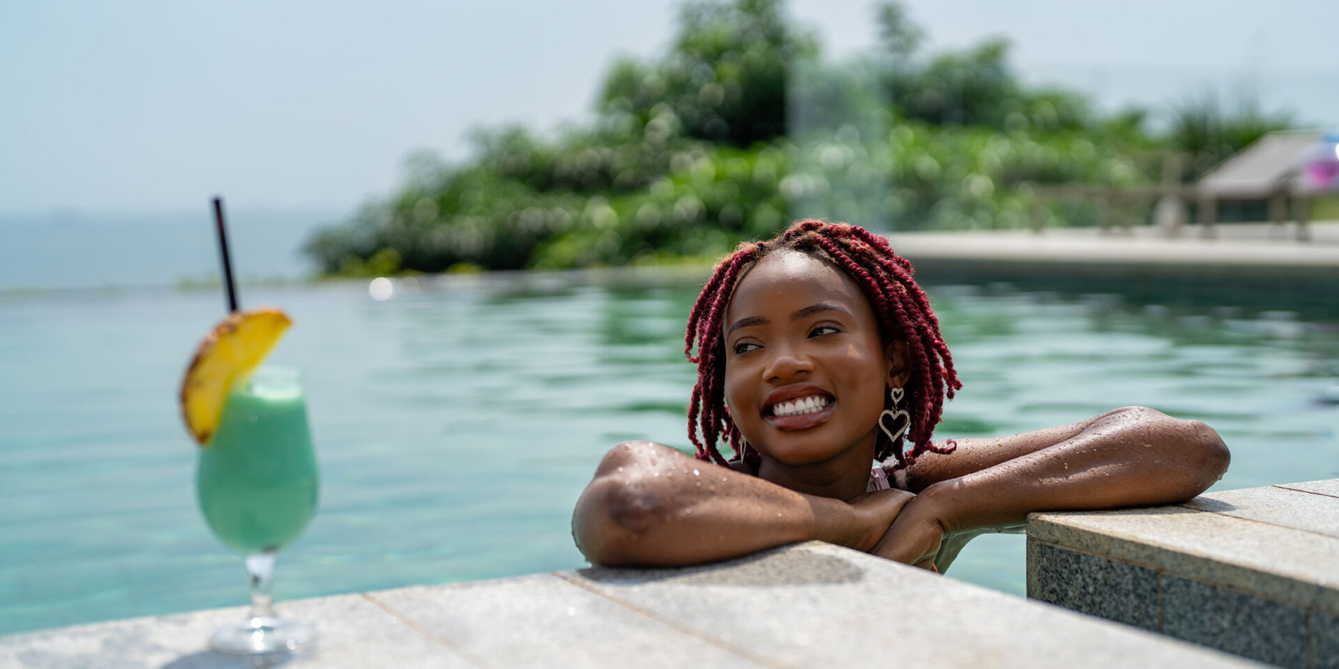 une femme se tient à côté d'une piscine avec un cocktail bleu à côté d'elle