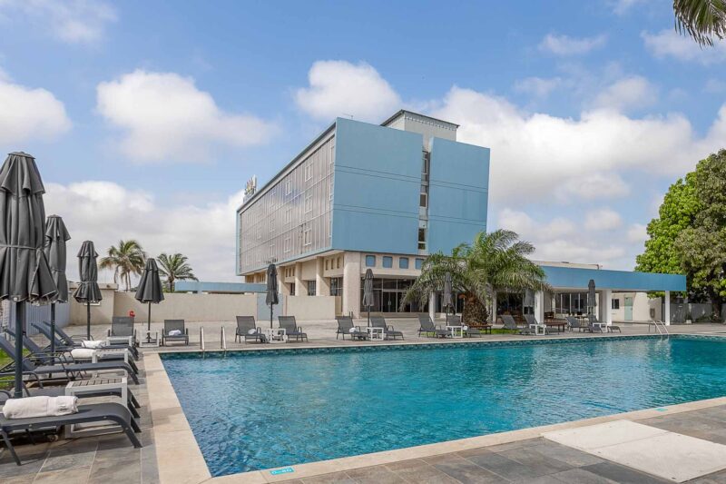 une grande piscine entourée de chaises et d' parasols avec un grand bâtiment en arrière-plan