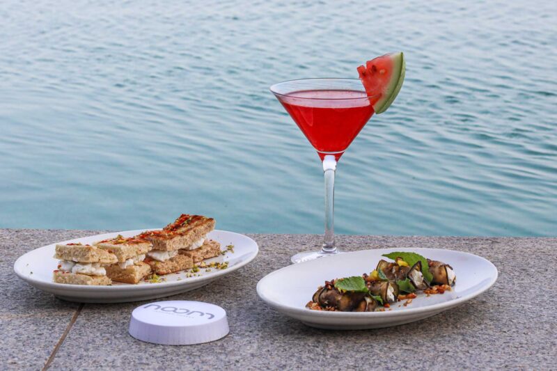 two plates of food next to a glass of red liquid with a watermelon slice on top