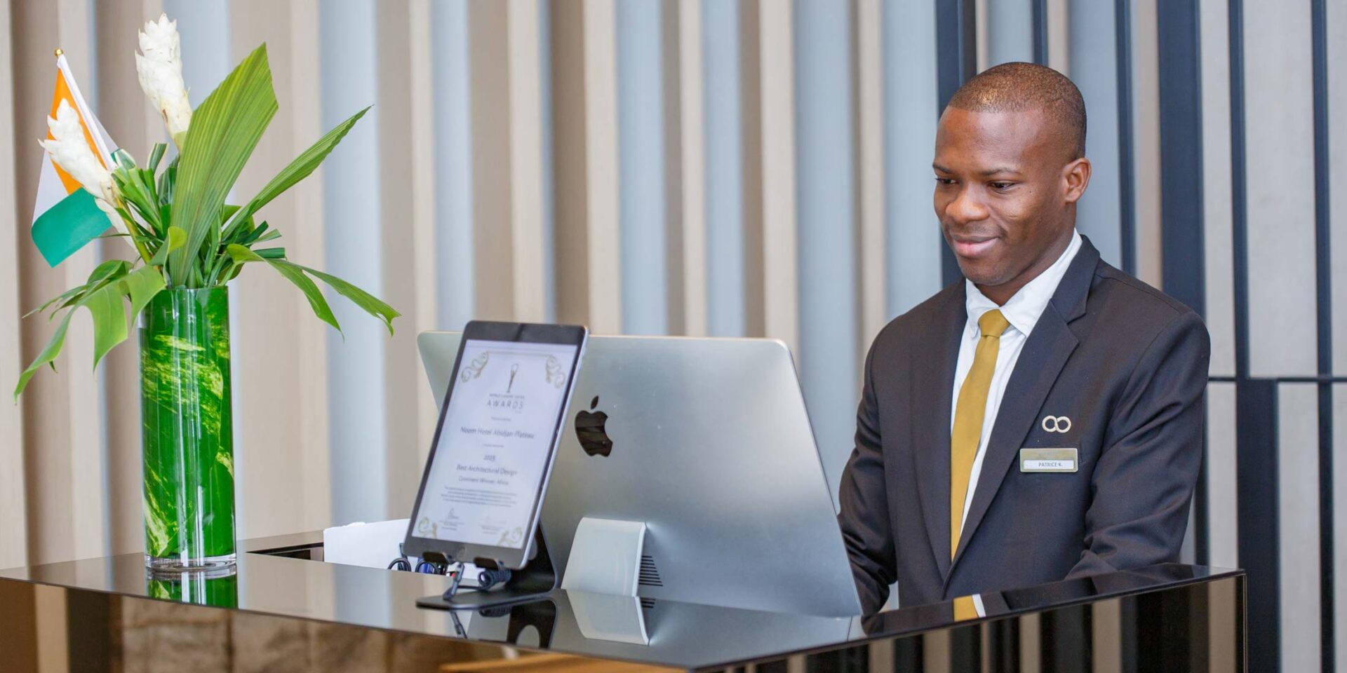 un homme en costume et cravate se tient devant un ordinateur apple