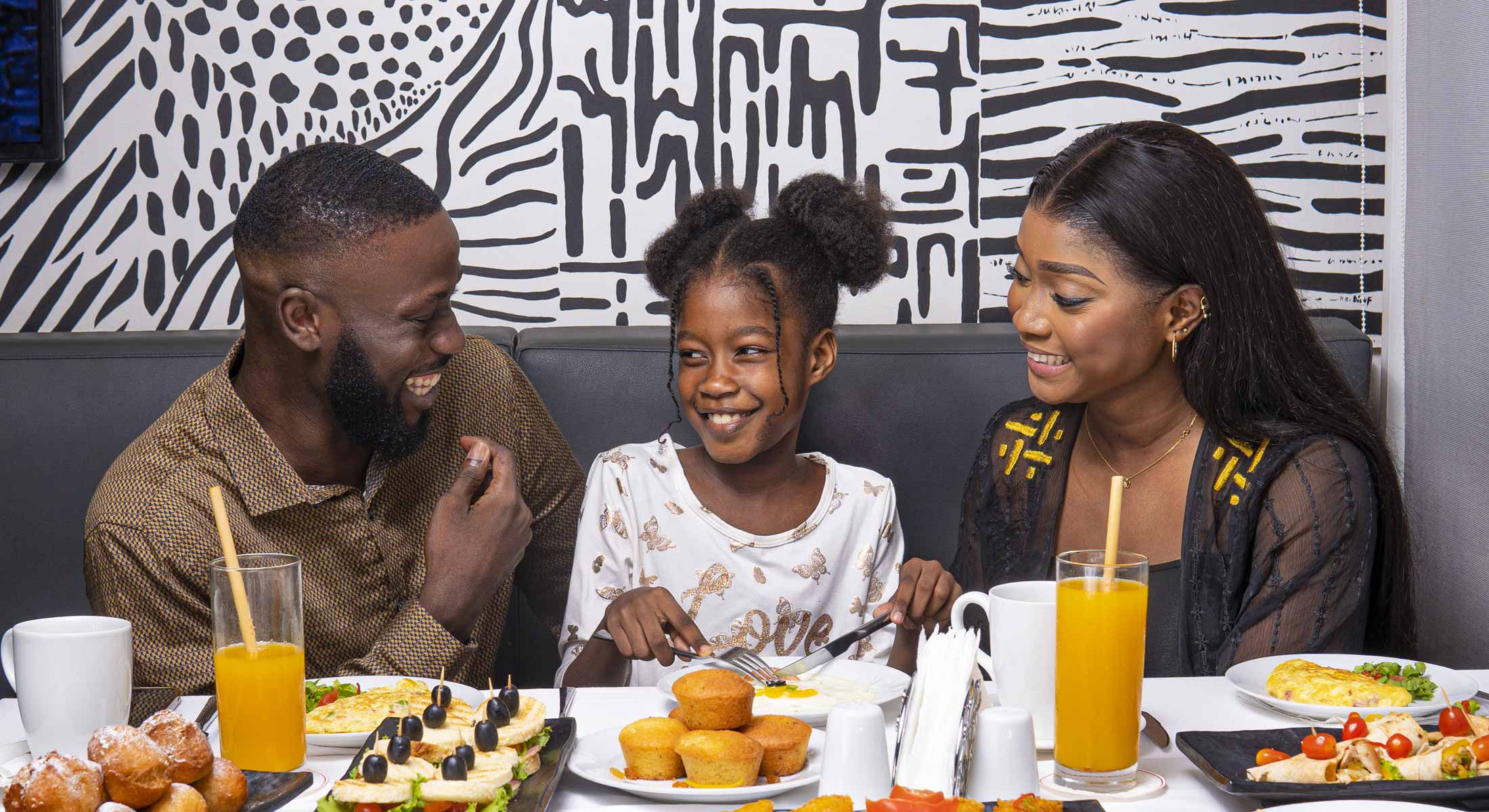 une famille assise à une table avec des assiettes de nourriture et du jus d'orange