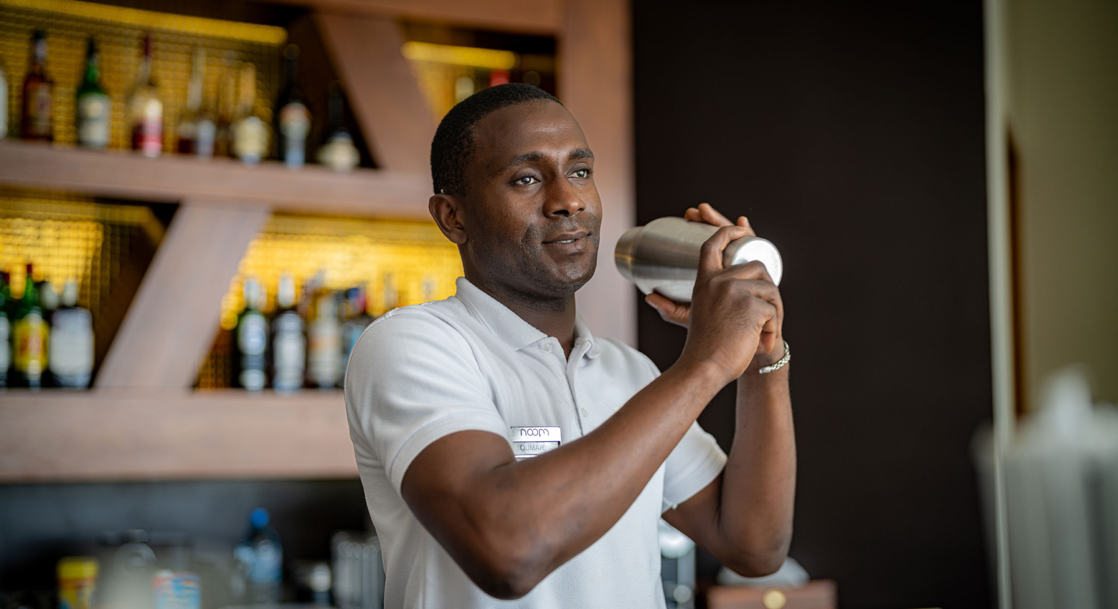 un homme en chemise blanche prépare un cocktail dans un shaker