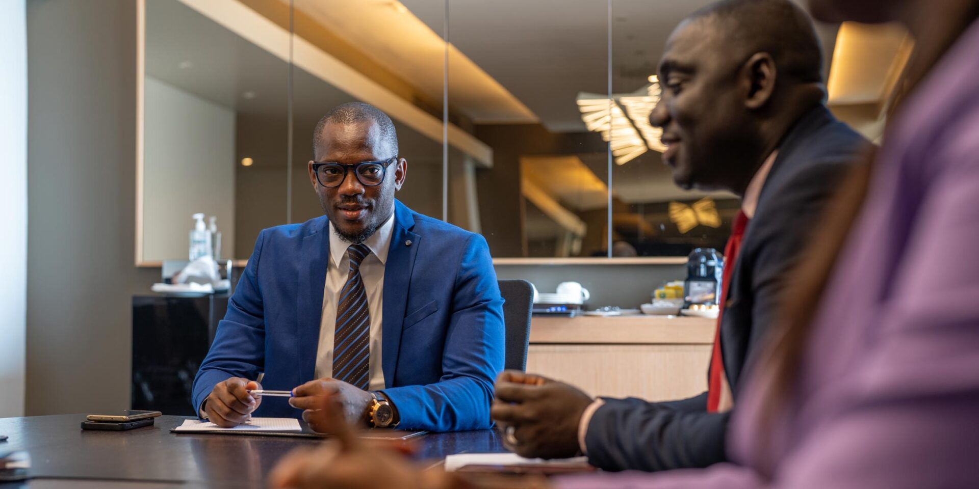 a man in a blue suit sits at a table with two other men